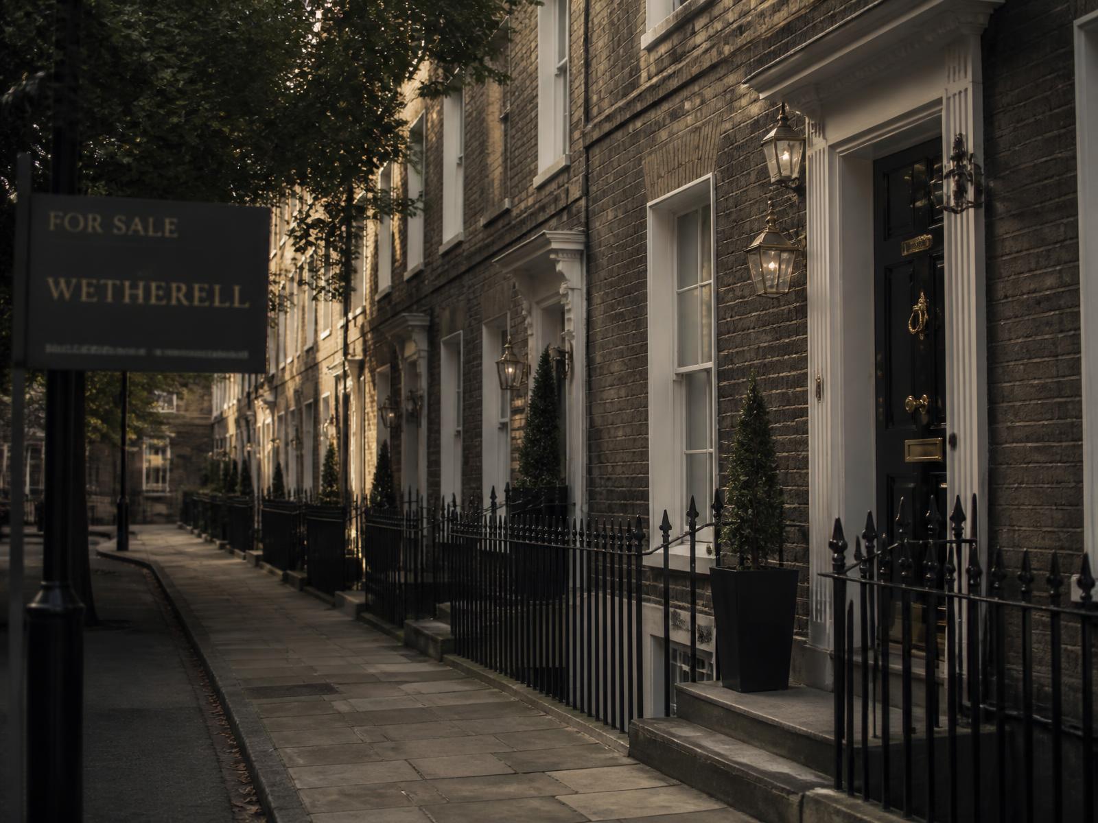 A row of period British townhouses at dusk with a for-sale board outside